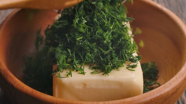 Freshly chopped green dill is sprinkled onto a block of soft butter in a wooden bowl. A key step in creating a flavorful homemade garlic and herb butter, perfect as a savory spread or for cooking