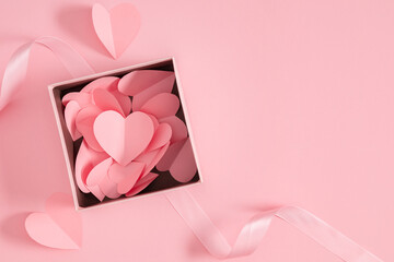Pink paper hearts in a gift box on a soft pink background with a ribbon. A composition for Valentine's Day, a wedding, or an anniversary with space for text. Valentine's Day hearts.