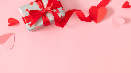 Valentine's Day background. Gift box with red ribbon and paper hearts on a soft pink background. Valentine's Day composition with copy space.