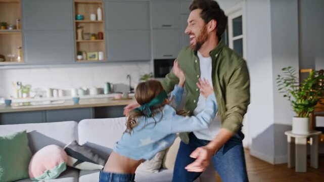 Cute girl catching father wearing blindfold home. Laughing daddy playing child