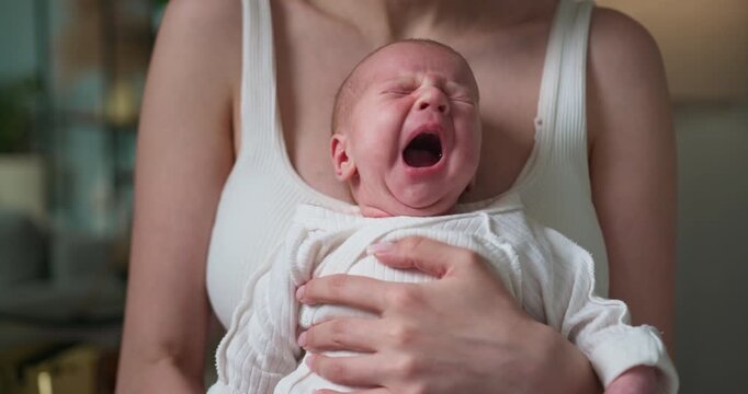 Mother cradles distressed infant, baby's face contorted in loud cries, expressing discomfort or hunger. Crying Newborn Baby Held By Mother