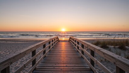 Fototapeta premium Wooden boardwalk leading to the ocean at sunrise. Symmetrical beach path during golden hour. Coastal landscape with sun on horizon