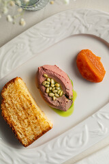 Restaurant style liver pate served with toasted bread pine nuts and fruit garnish on white plate