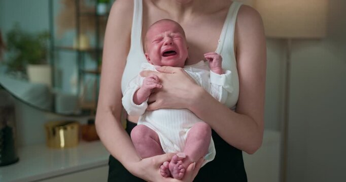 Mother holds distressed infant with red face and open mouth, showing discomfort and need for attention. Newborn Baby Crying in Arms