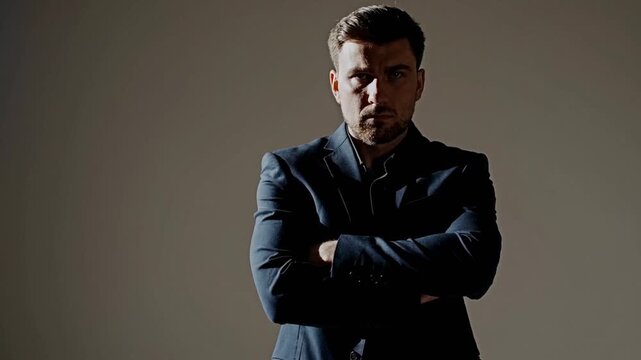 A man in a suit is standing in front of a wall, looking away from the camera. He is wearing a tie and has his arms crossed. Concept of formality and seriousness