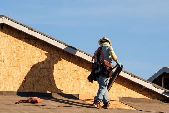 Construction worker installs roofing underlayment on a wood framed house under construction, illustrating residential roofing preparation and weatherproofing prior to final roof covering