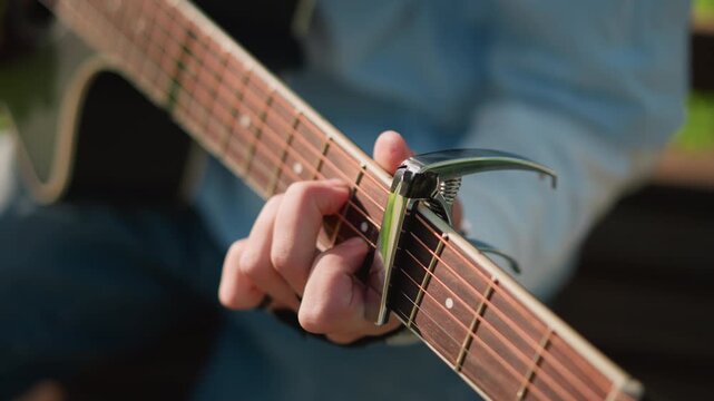 closeup capo change on guitar, energetic practice session showing capo shifting and chord transitions, hands adjusting fretboard with precision, denimclad player demonstrating shapes, outdoor park