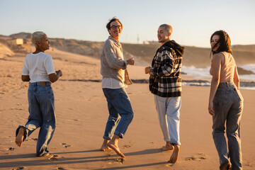 Diverse friends walking barefoot on sandy beach looking back