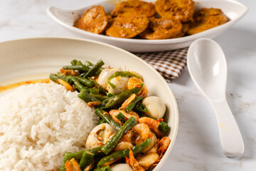 Fototapeta premium White rice with shrimp tauco and quail eggs with long bean vegetables on a white plate and a plate of jengkol kalio on a napkin.