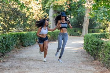 Fototapeta premium Two latin women athletes running together in a park holding hands