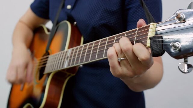 Closeup of caucasian woman fingers pressing strings on acoustic guitar fingerboard indoors. Symbolizing music learning, skill development and instrumental practice.