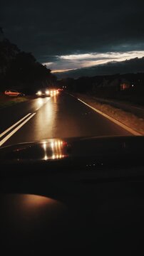 Vertical shot of a car driving through a pedestrian crossing on a wet asphalt road in Poland during twilight. Oncoming traffic with headlights on