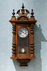 Rich wooden wall clock hangs on the wall in a room with light blue wallpaper