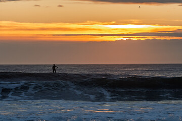 Fototapeta premium Sunrise over Atlantic Ocean on the New Jersey Shore with the silhouette of an stand up paddle boarder in the distance on other side of waves