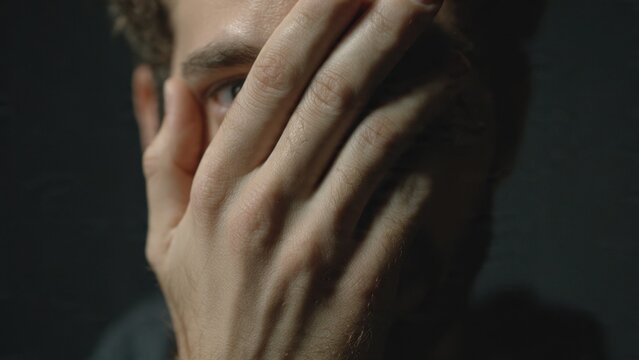 Man covering face with hand in dark