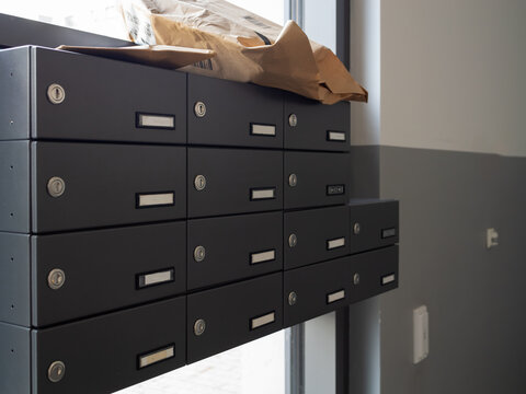 Modern dark grey communal mailboxes stack in apartment building lobby with delivered parcel on top, close-up, security, organization, and the modern mail delivery process.