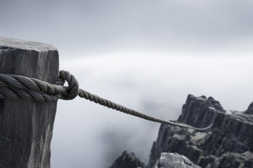 Fototapeta premium Rope tightly secured to a weathered wooden post at the cliff's edge, stretching into a foggy abyss, evoking a sense of isolation and mystery