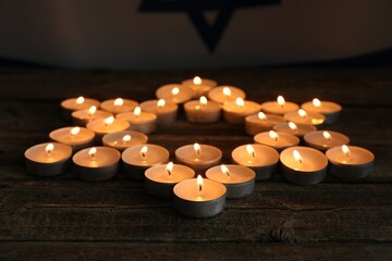 Holocaust Remembrance Day. Burning candles in shape of Star of David on wooden table, closeup