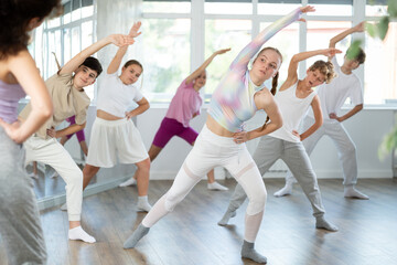 Obraz premium Girl teen performs modern dances repeats movements of unrecognizable teacher together with friends during lesson at choreographic school. Hobbies, active pastime