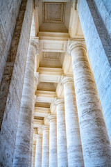 Naklejka premium The view shows tall columns in a colonnade at St Peters Square in Vatican. The structure highlights classic architecture and historical design. Light comes through the columns creating a unique view.