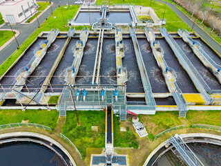 Wastewater treatment facility processes water using several large tanks and channels with flowing water on a sunny day