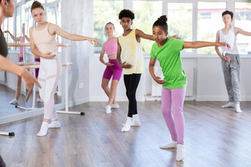 Fototapeta premium Thin teen girl doing choreography together with other juvenile participants of ballet classes
