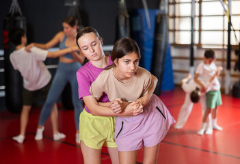 Fototapeta premium Teen girls train in pairs to strike and reflect blows of enemy. Self-defense training and Krav Maga principles, physical activity, sports self-defense classes...