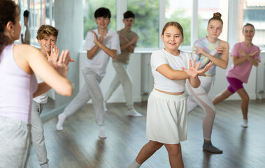 Teenage girl rehearse hip hop dance repeats movements of unrecognizable instructor performance with peers. Preparing for performance of choreographic team, practicing skills, repeating exercises