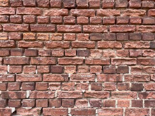 Naklejka premium Red brick wall texture with uneven surface and mortar joints, showcasing a rustic appearance suitable for architectural and design backgrounds