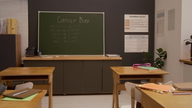 Zoom in shot of empty school classroom focus flowing from rows of wooden desks to blackboard with words Career Day, copy space