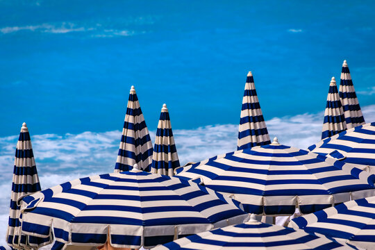 Striped umbrellas on a beach along Promenade des Anglais with the turquoise water of the Mediterranean Sea in the background in Nice, South of France