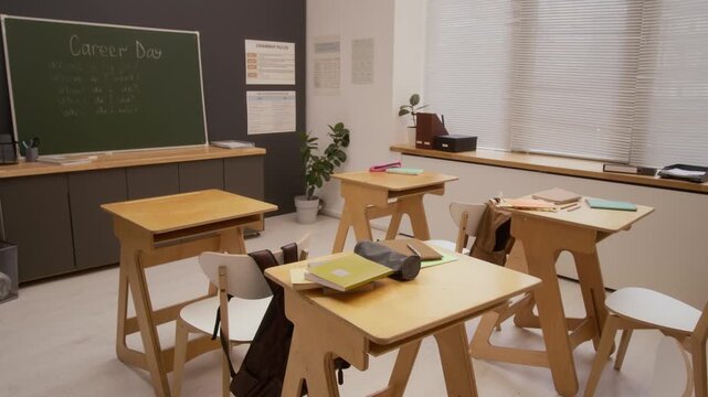 Pan left wide angle shot of empty school classroom with wooden desks focus flowing to words Career Day written on blackboard, copy space
