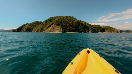 Front of a kayak on blue sea water with an island in the background 