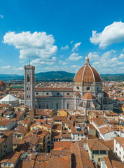 Fototapeta premium Aerial view of Florence Duomo rising above the historic city center, surrounded by red rooftops and Renaissance architecture under a clear blue sky on a sunny summer day in Italy
