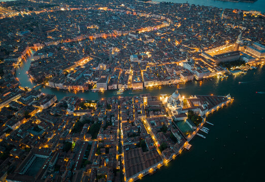 Aerial view of Venice historic city at night showing the Grand Canal, glowing canals and dense urban fabric. Illuminated architecture highlights the unique layout of Venice, Italy
