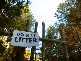 Fototapeta premium Low-angle shot of a 'DO NOT LITTER' sign attached to a wooden fence in a forest with trees and a sunny sky.