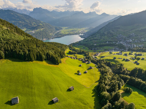 Scenic aerial view of an alpine valley near Walensee in St Gallen, featuring green meadows, scattered farmhouses and dramatic mountain terrain in Switzerland