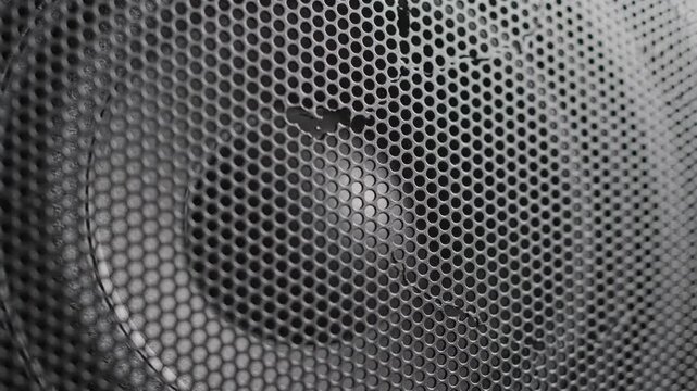 Close view of a speaker cone pulsing with deep bass, monochrome image of a loudspeaker woofer behind a metal mesh grille, audio equipment and sound technology concept, realistic style.