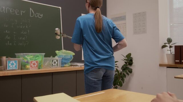 Close up shot of young woman as environmental educator demonstrating litter picker tool and putting can in sorting bin while giving presentation on career day in school
