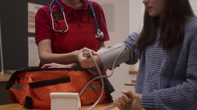 Tilt up shot of young woman as female paramedic using blood pressure monitor on smiling young girl while giving interactive presentation to group of children on career day in school