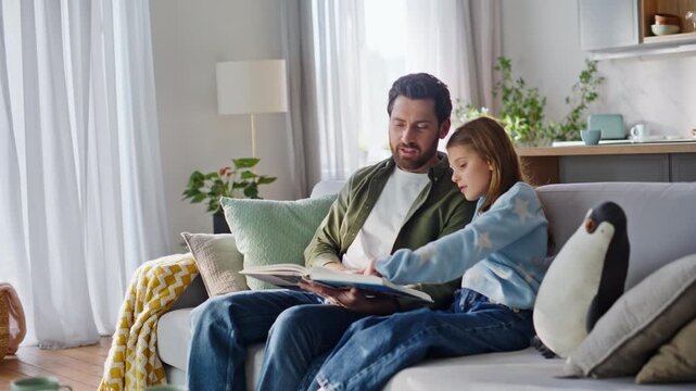 Dad daughter enjoying book feeling togetherness home couch. Father reading girl