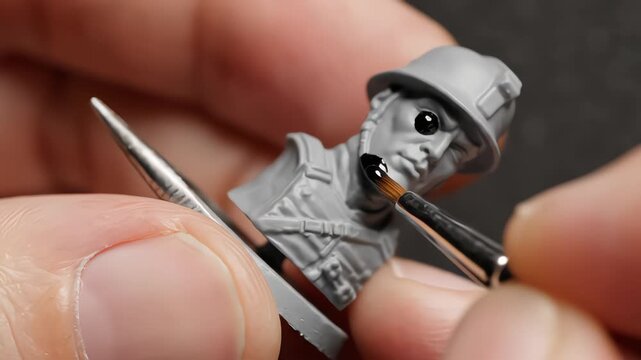Macro shot of artist painting grey resin soldier miniature bust with fine brush, applying detail to face under bright studio light, showcasing hobbyist precision and craftsmanship