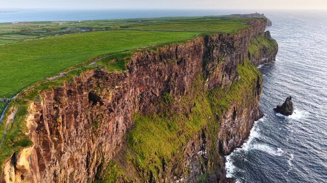 Majestic Cliffs of Moher rising vertically from the Atlantic Ocean on a misty day. Cinematic aerial drone footage of the rugged Irish coastline and crashing waves, County Clare, Ireland. 4K