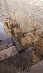 Obraz premium Reflection of a church facade in a puddle on old cobblestone pavement on a sunny day.