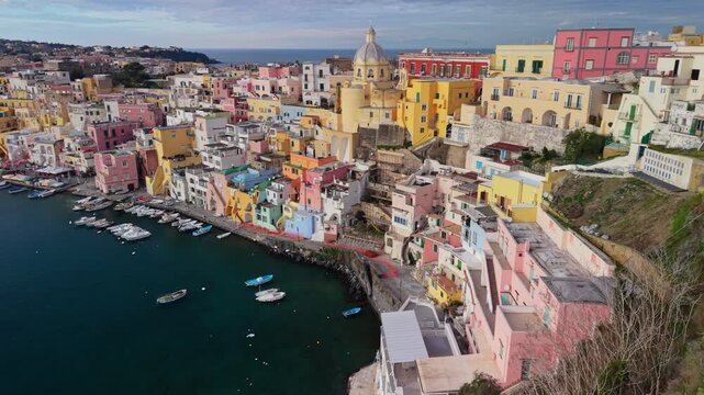 Breathtaking panorama of colorful fishing village Marina di Corricella from drone perspective. Spectacular aerial footage of vibrant pastel houses and boats in harbor, Procida Island, Naples, Italy