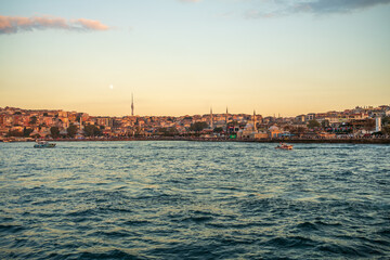 Fototapeta premium Golden-hour view across Bosphorus toward Uskudar waterfront, Istanbul, Turkey with Camlica Tower left, Mihrimah Sultan Mosque and Semsi Ahmet Pasha Mosque right against clear sky