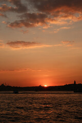 Naklejka premium Sunset across the Bosphorus toward Eminonu and Karakoy, with silhouettes of Suleymaniye and Fatih Mosques and the Galata Tower against orange sky in Istanbul, Turkey