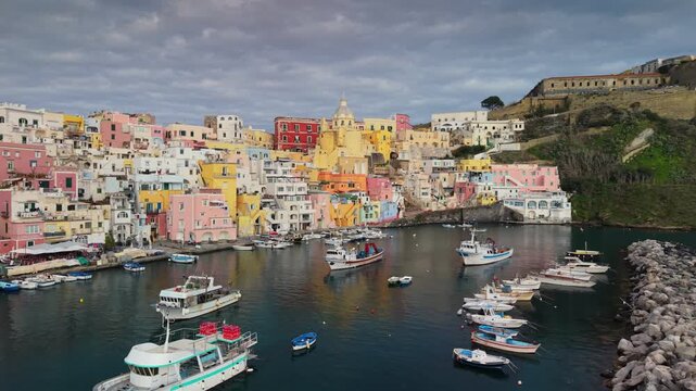 Spectacular wide-angle drone flyover of the ancient fortress and vibrant Corricella harbor. Majestic cinematic panorama of the colorful island architecture and turquoise sea, Procida, Naples, Italy