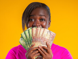 A woman in a pink top smiles excitedly behind a fan of Kenyan Shilling notes. Set against a vibrant yellow background, the image captures a moment of joy, financial success, and celebration.