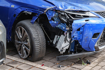 Severely damaged modern blue car front showing collision impact, broken panels and exposed parts